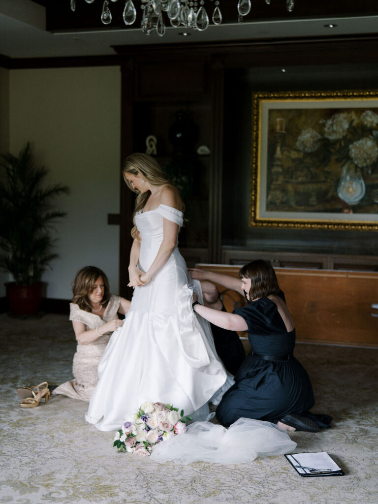 Bride getting her dress adjusted by her mother and the wedding planner