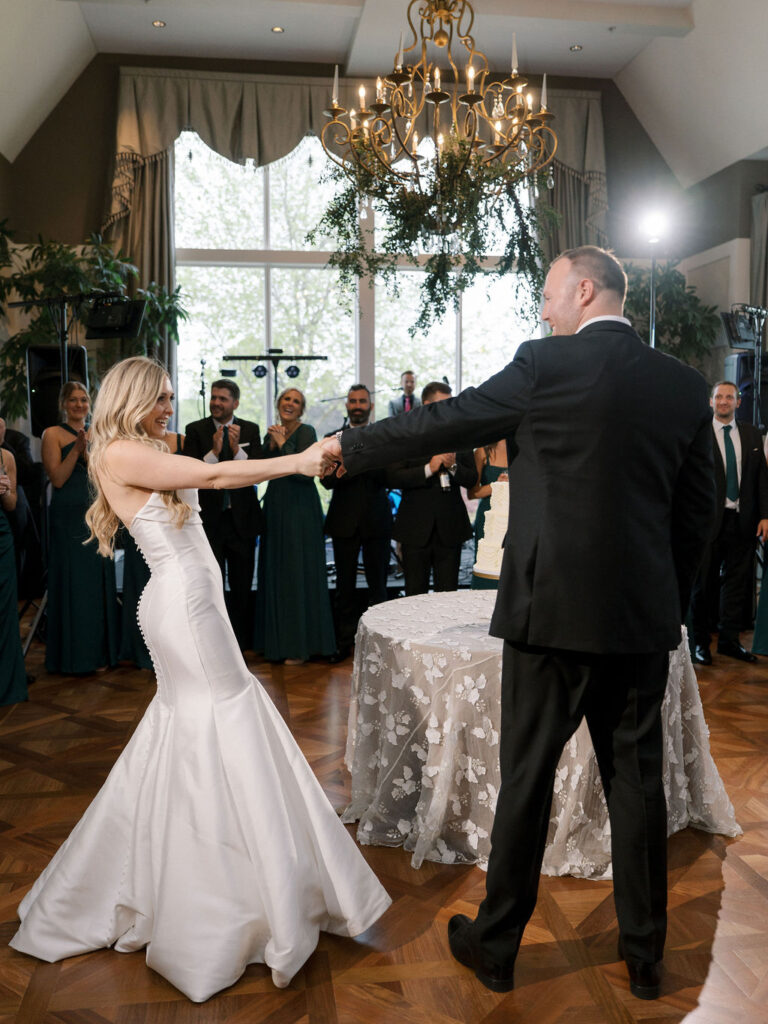 Bride and groom share their first dance beneath a stunning crystal chandelier in the Cascade Hills Country Club ballroom.