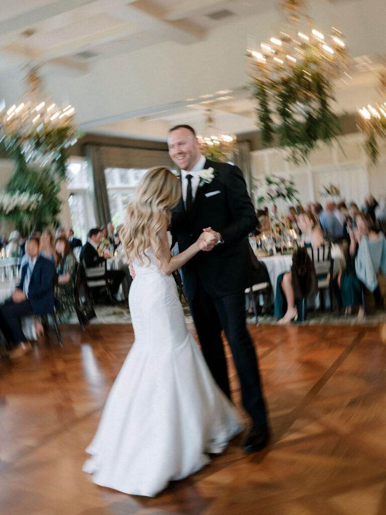 Bride and groom share their first dance beneath a stunning crystal chandelier in the Cascade Hills Country Club ballroom.