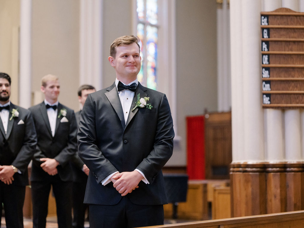 Groom smiling as he watches his bride walking down the aisle towards him