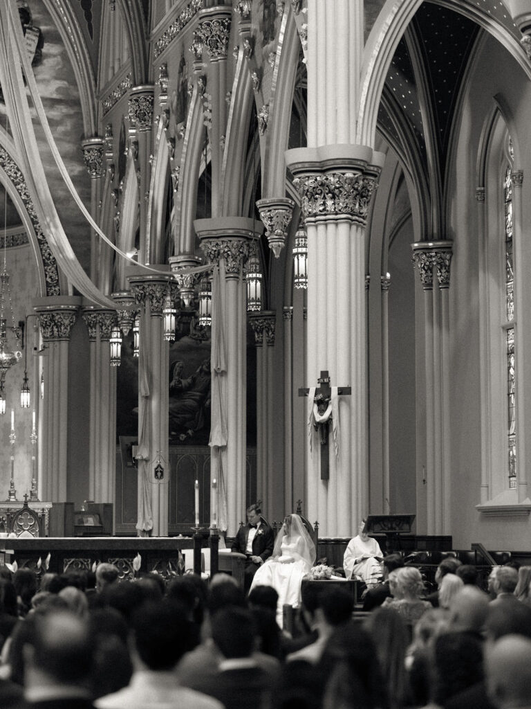 Black and white photo of a bride and groom sitting during their Notre Dame Basilica wedding ceremony