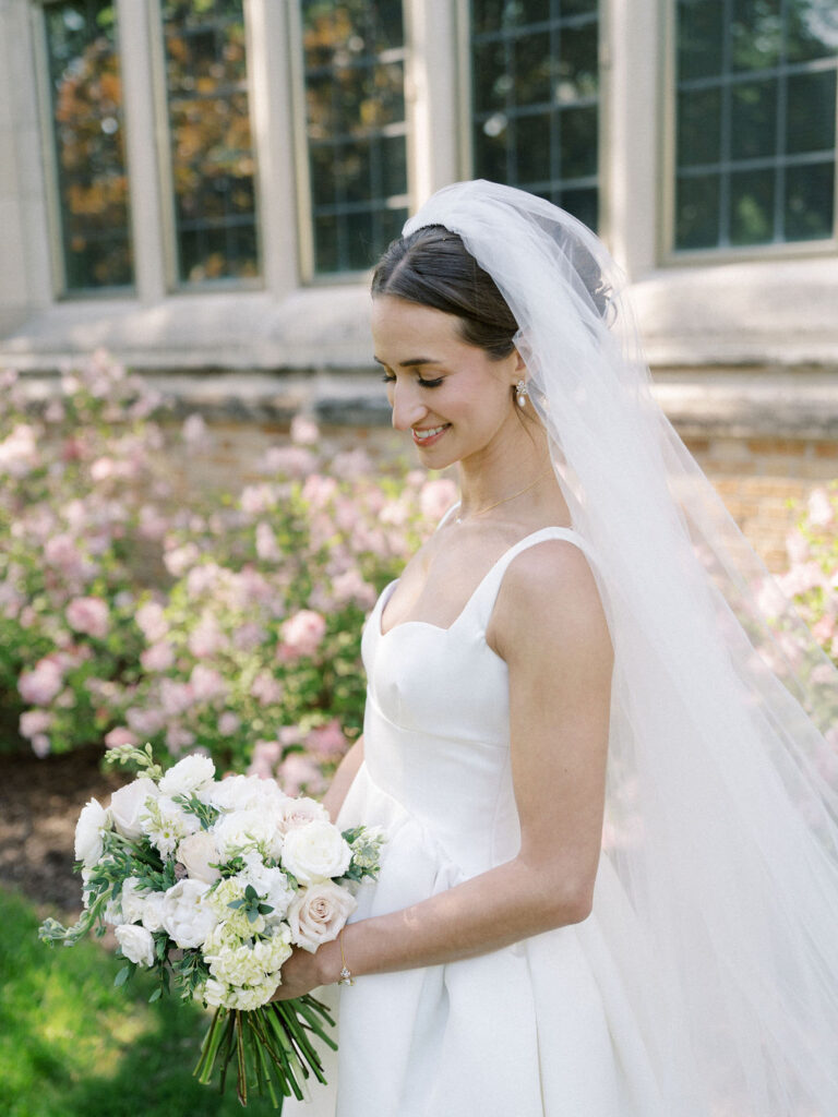 Portrait of the bride in her veil holding a white floral bouquet against a backdrop of pink flowers