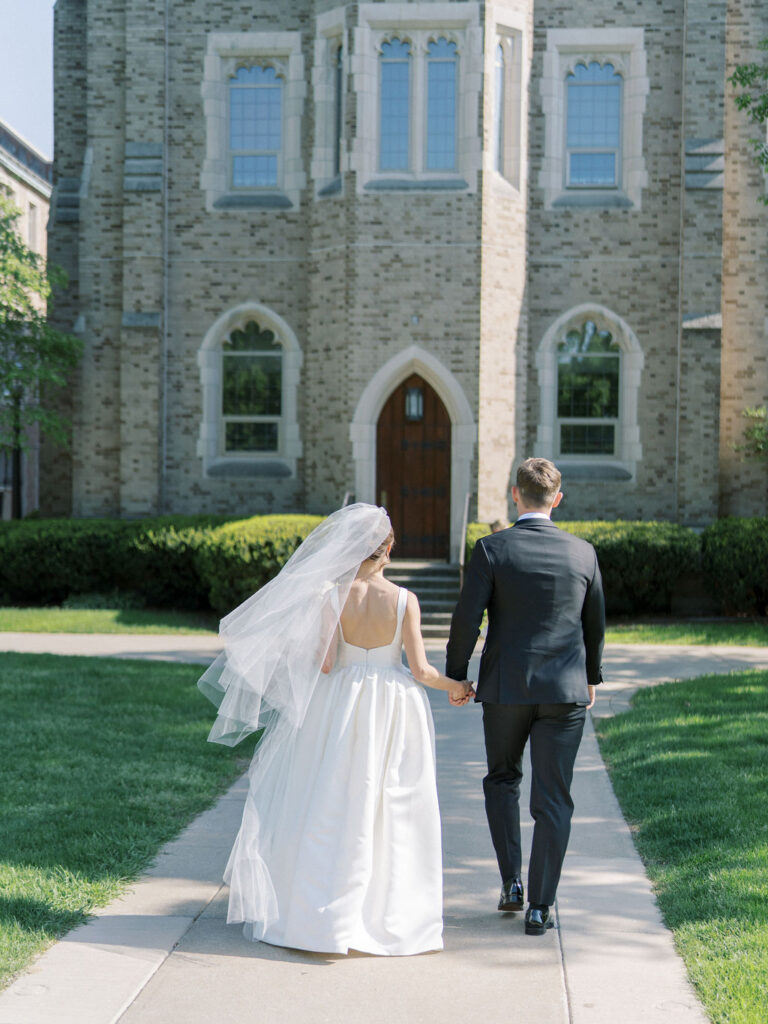 Bride and groom walking hand-in-hand down a sidewalk toward the iconic Notre Dame architecture