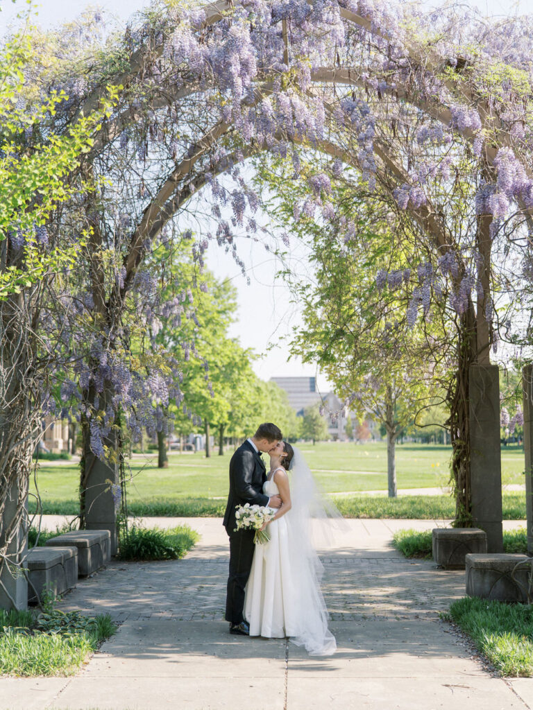 The couple sharing a quiet moment beneath a flowering archway on campus for their Notre Dame wedding photos
