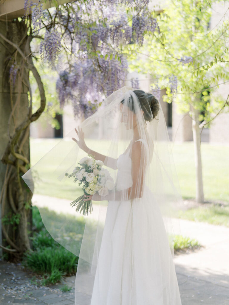 Bride holding her bouquet beneath soft, flowing veil under blooming vines
