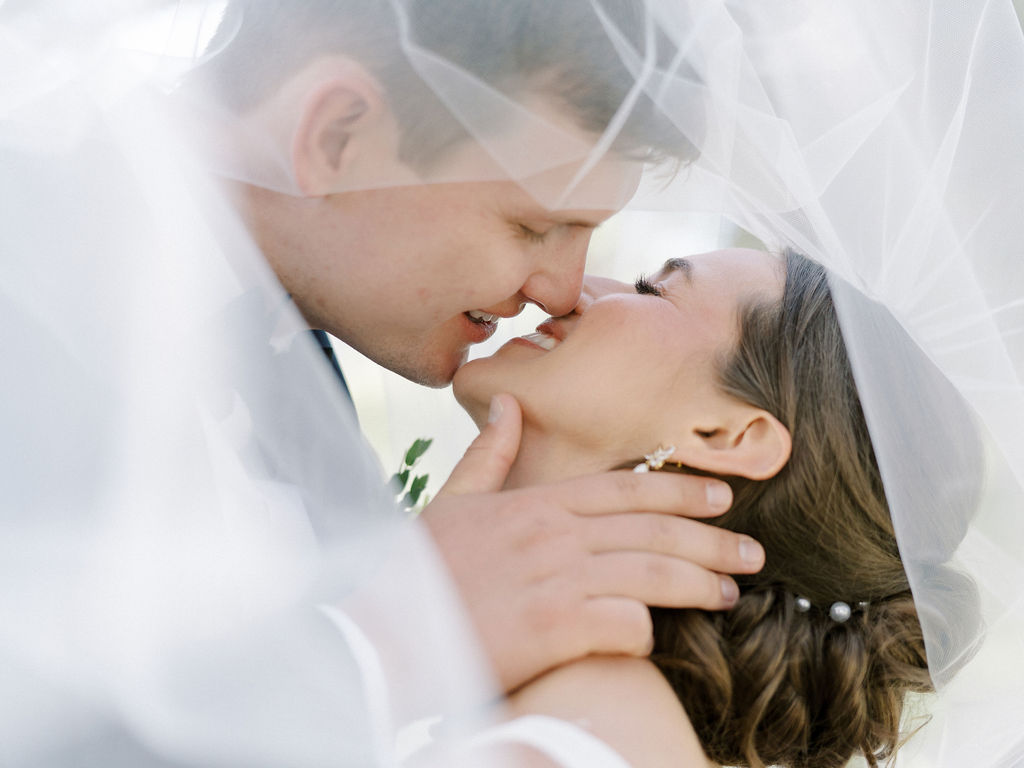 Couple kissing under the brides veil for their romantic Notre Dame wedding photos