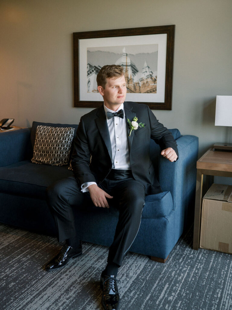 Groom sitting in a suit on a navy couch, looking out before ceremony