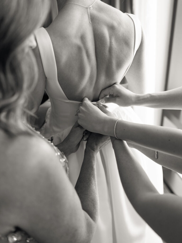Black and white photo of a bride getting her dress zipped up
