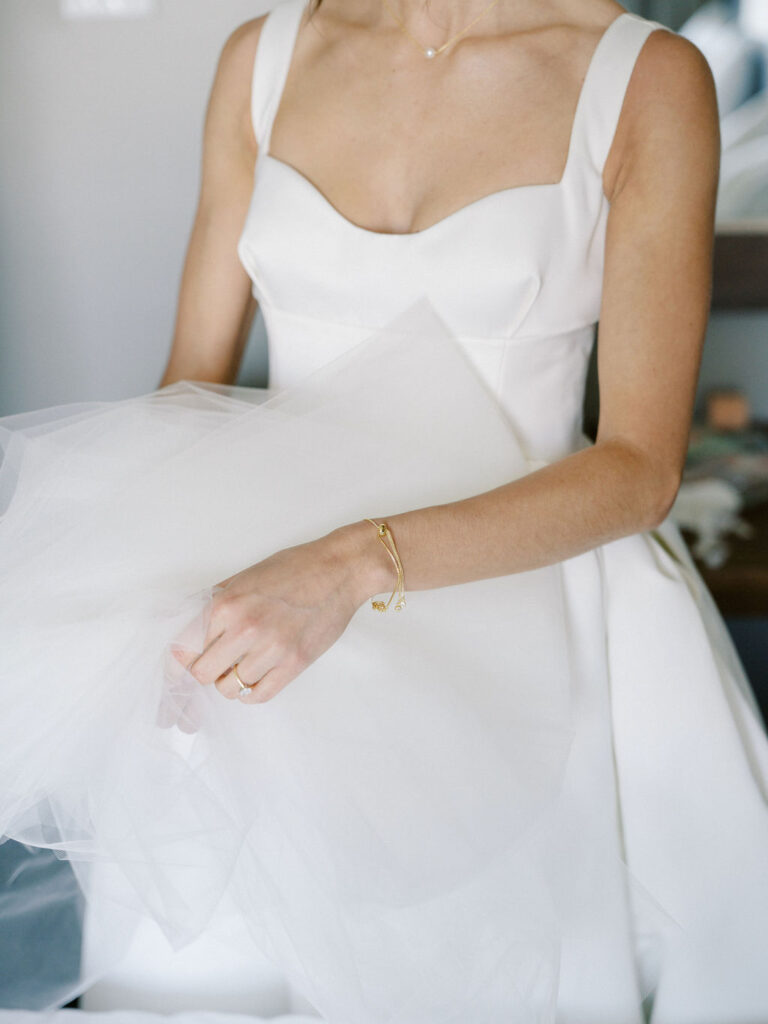 Close-up of bride’s gown and jewelry as she holds her veil

