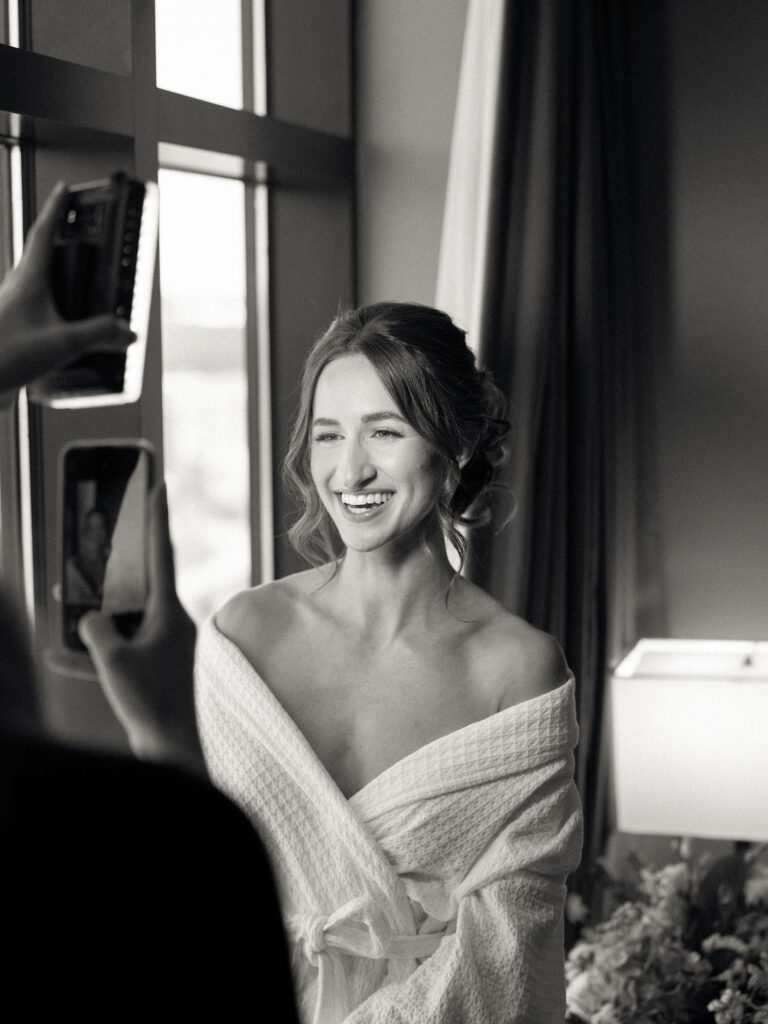 Black and white photo of the bride smiling in a robe during wedding prep