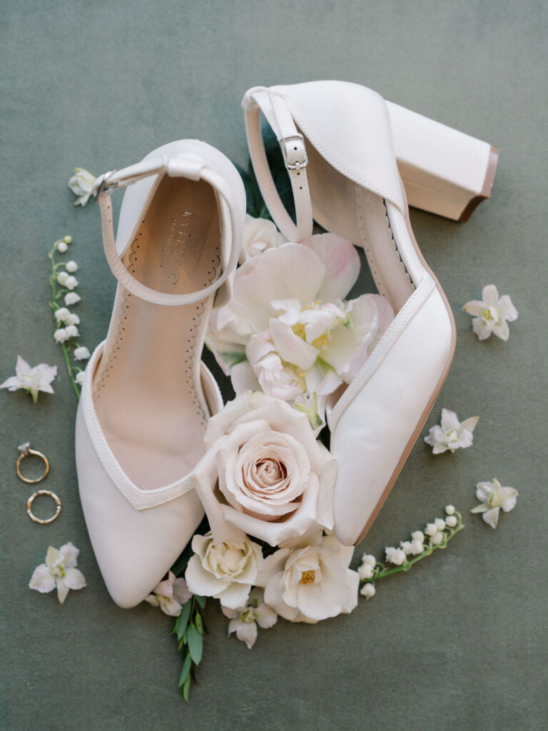 Wedding detail shot of a brides heels with her wedding rings and florals
