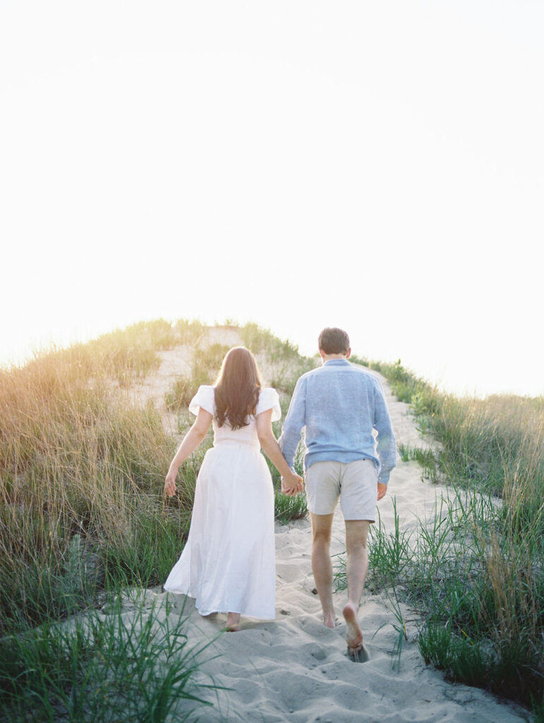 Couple holding hands and walking up a hill at Warren Dunes State Park for their Michigan engagement photos