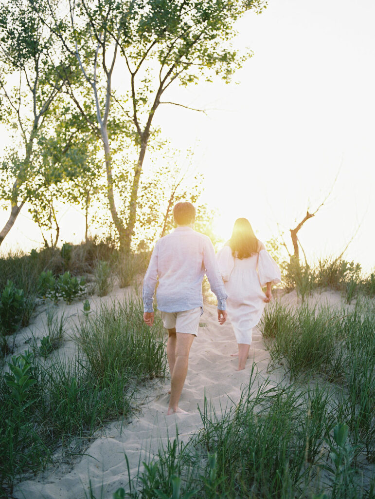 Film engagement photo of a couple walking up a beach hill at sunset