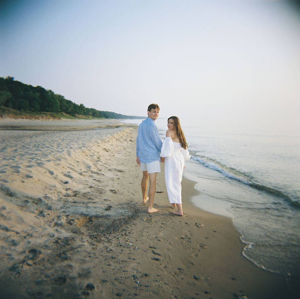 Couple walking the shoreline at Warren Dunes State Park in Michigan for their engagement shoot