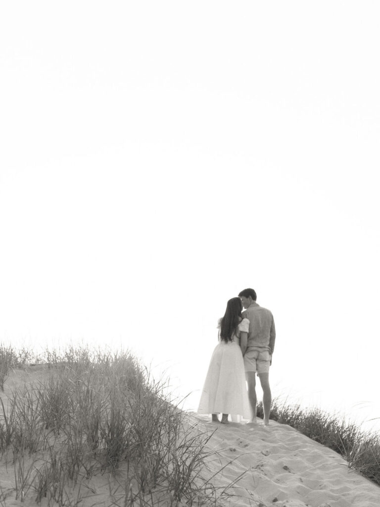 Black and white photo of a couple kissing on top of a sand hill