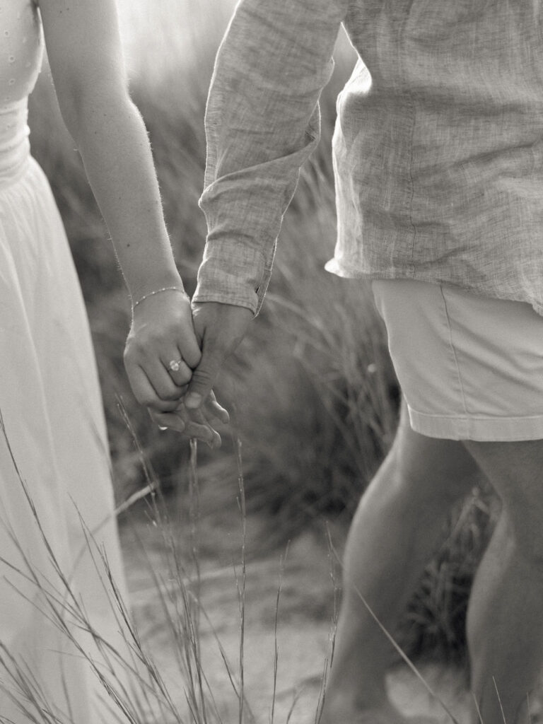 Black and white engagement detail photo of a couple holding hands at the beach