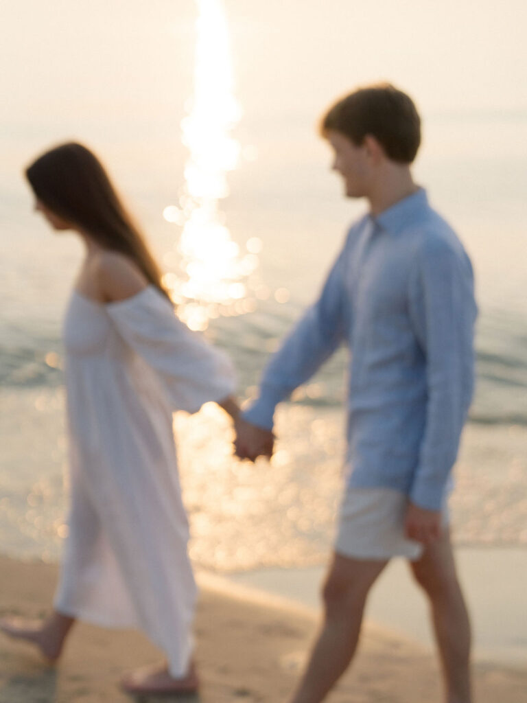 Out of focus photo of a couple holding hands and walking the shoreline at sunset