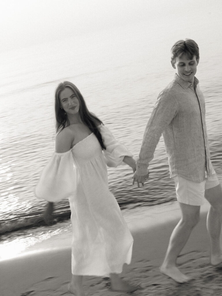 Flash black and white engagement photo of a couple running along the shoreline of Warren Dunes State Park in Michigan