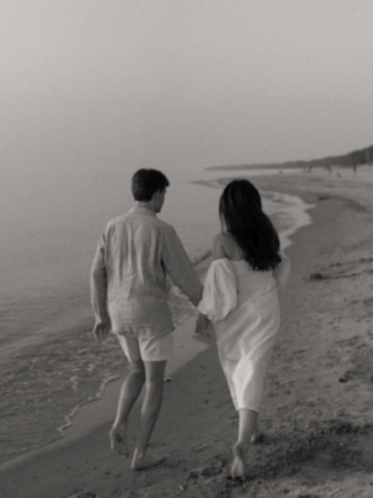 Black and white Michigan engagement photo of a couple running along the shoreline at Warren Dunes State Park in Michigan