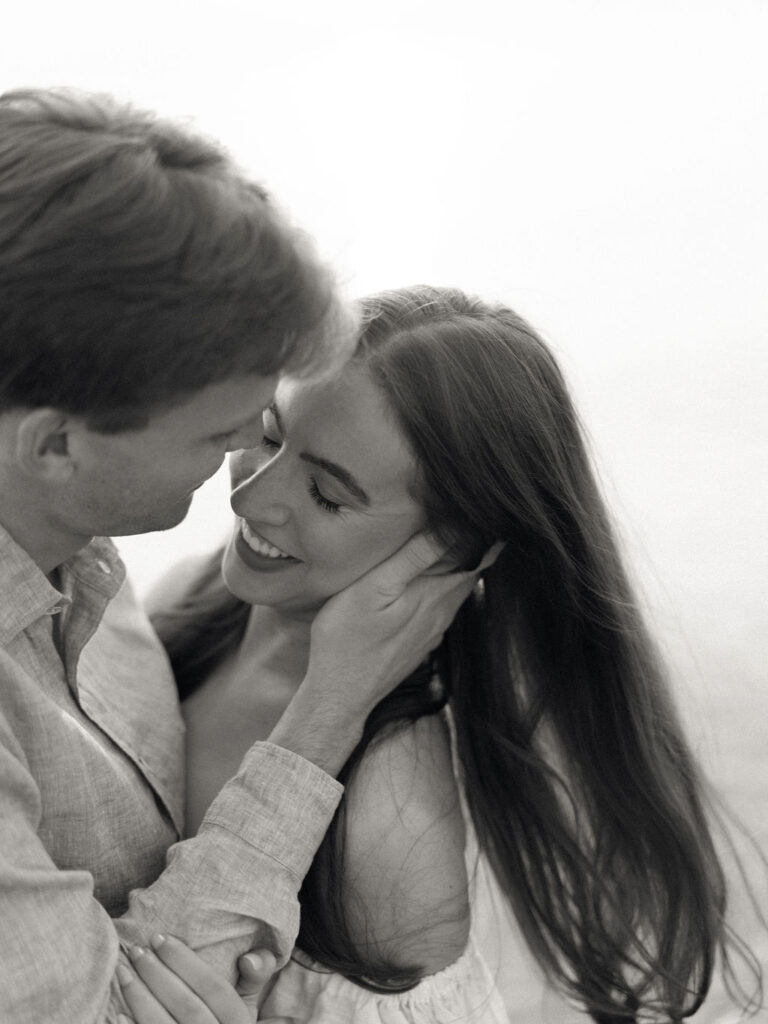 Black and white photo of a man caressing his fiancés face during their beach engagement session in Michigan