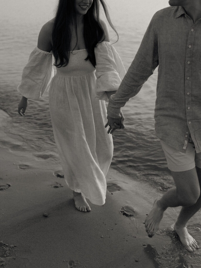 Black and white Michigan engagement photo of a couple running along the shoreline at Warren Dunes State Park in Michigan