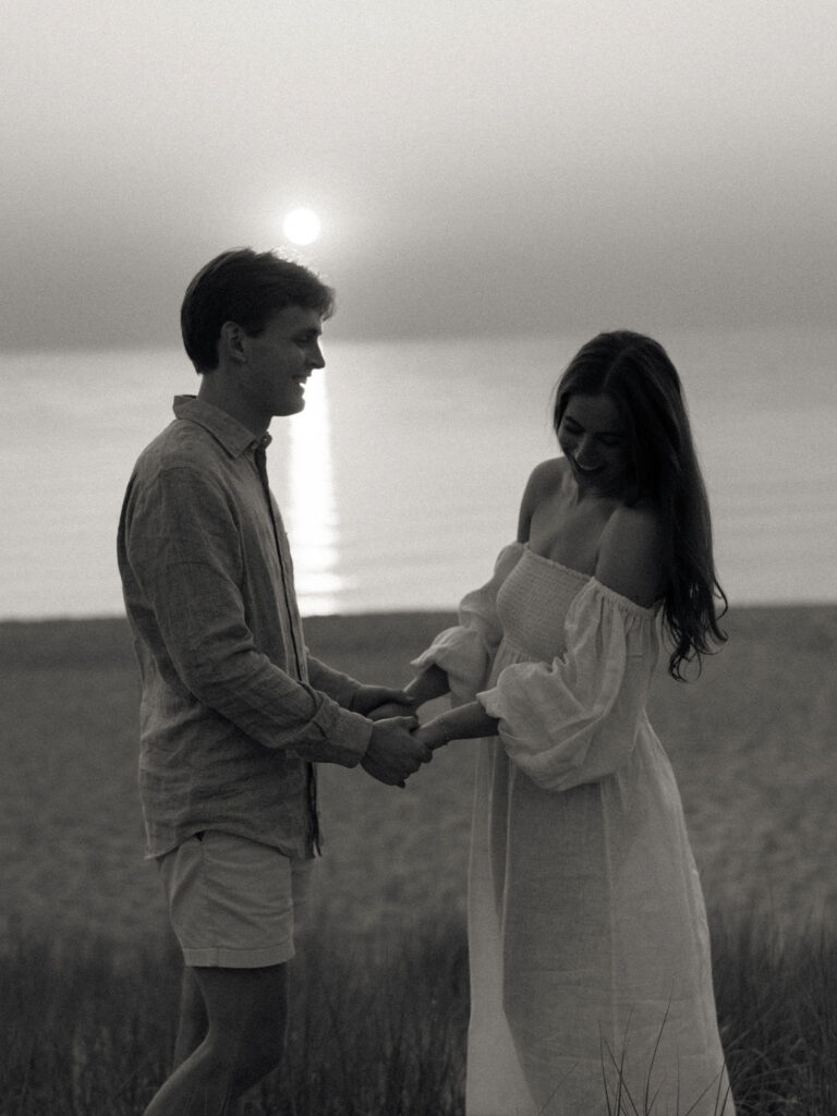 Black and white photo of a couple holding hands on the beach during sunset