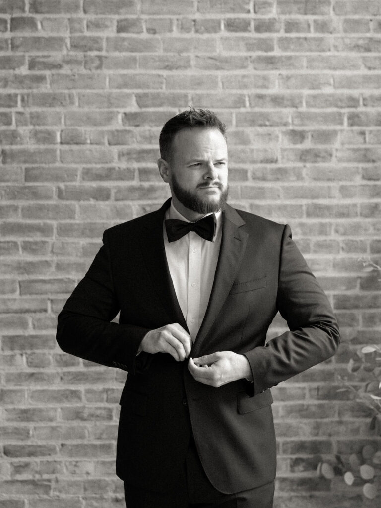 Black and white photo of the groom buttoning up his suit