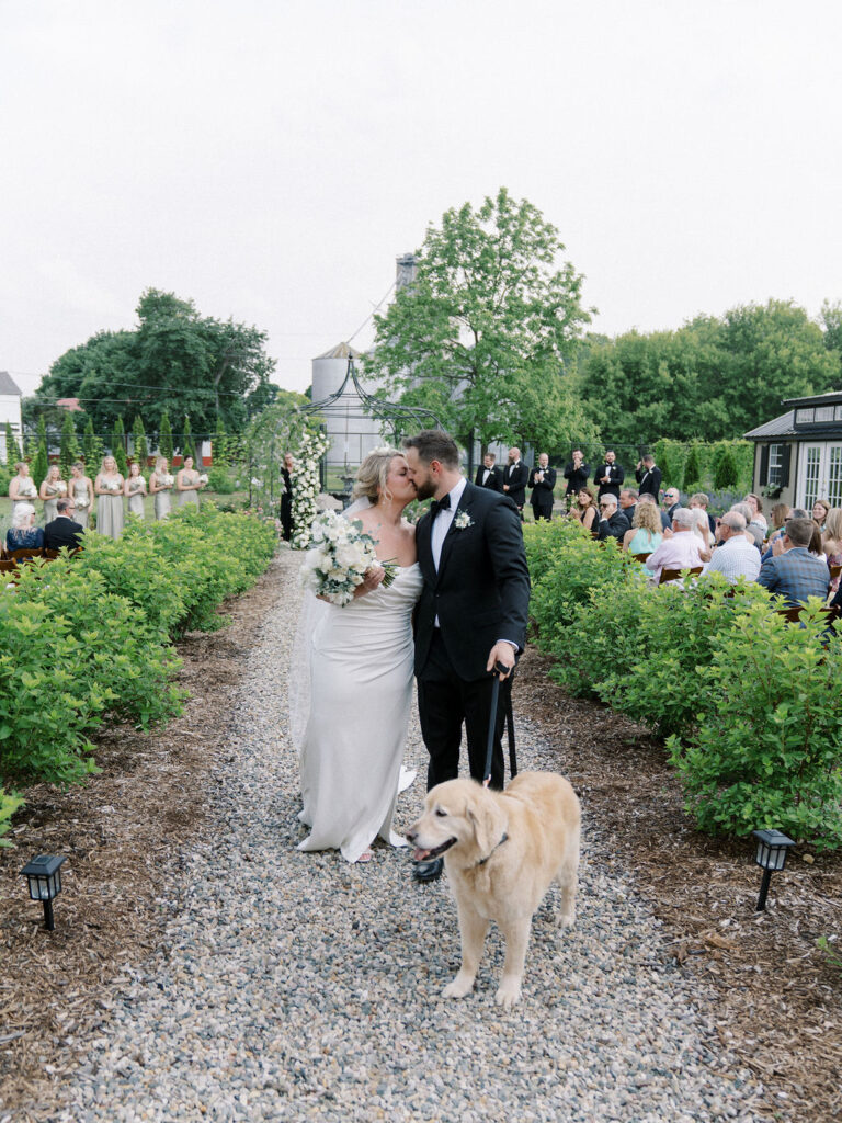 Bride and groom walking back down the aisle as husband and wife with their dog after their outdoor garden wedding ceremony at The Millhaven
