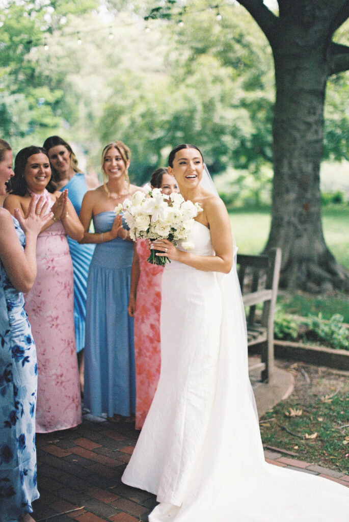 Bride surrounded by bridesmaids in pastel pink and blue dresses laughing together at Saint Mary’s College – Cynthia Mae Photo.