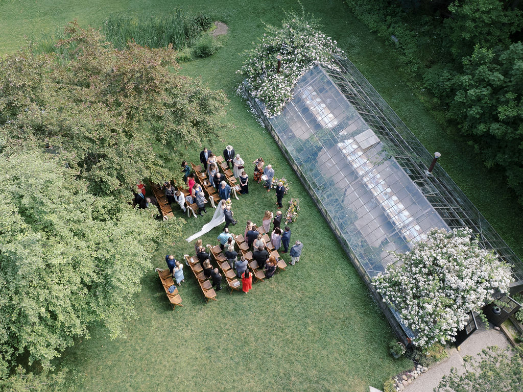 Aerial view of the bride walking down the aisle with the ceremony setup beside the greenhouse surrounded by lush greenery.