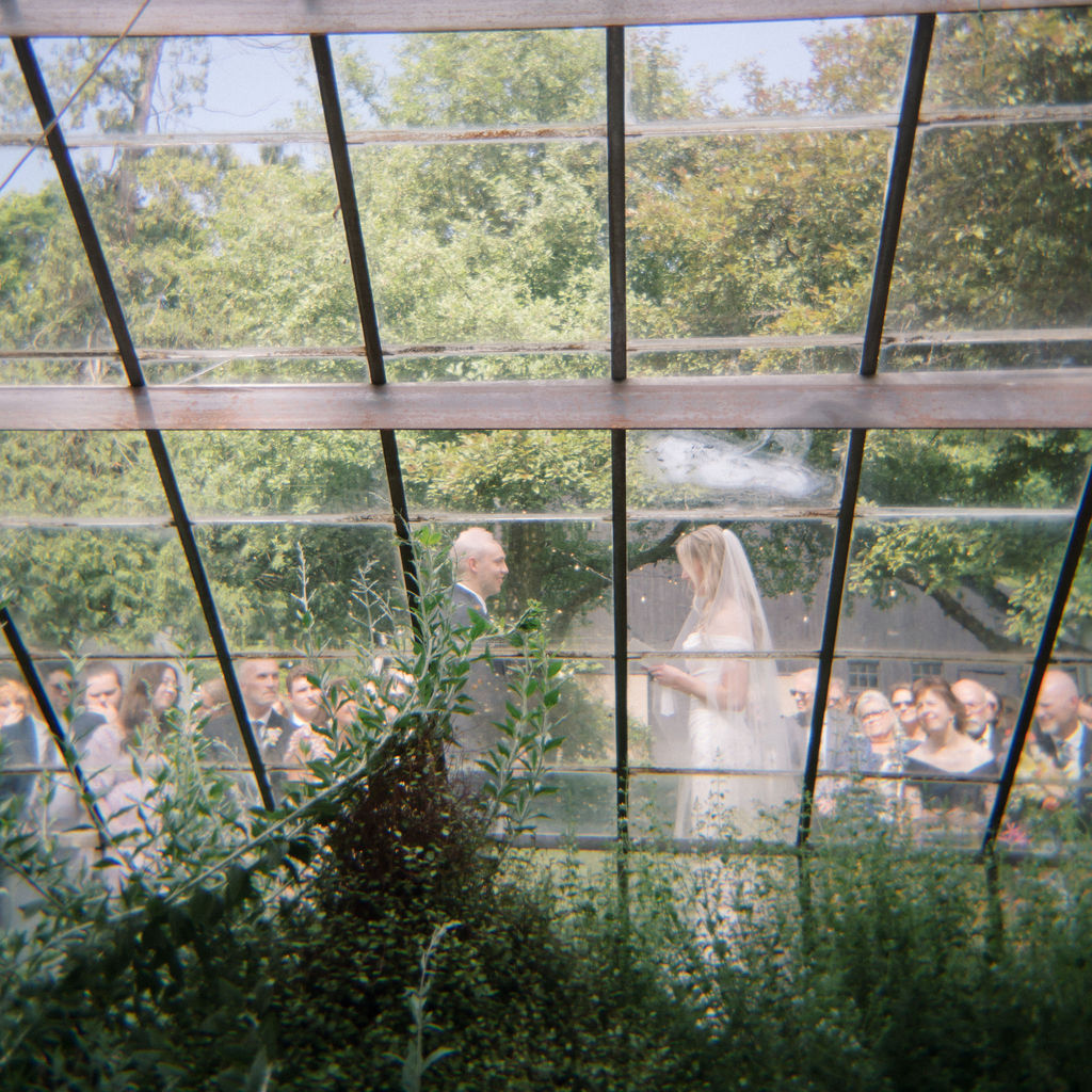 Bride and groom exchanging vows  seen through the greenhouse glass during the ceremony
