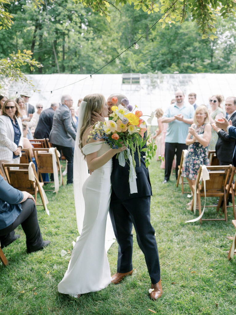 Bride and groom sharing a kiss at the end of the aisle as husband and wife after their Glass House Community wedding ceremony