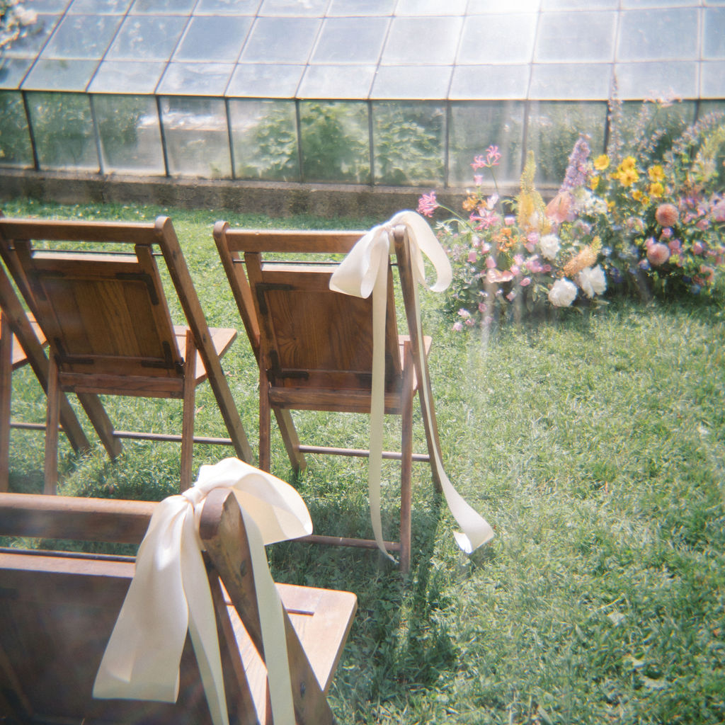 Wooden ceremony chairs tied with white ribbons in the grass.