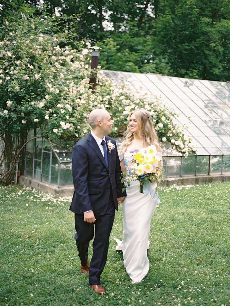 Bride and groom walking together for for their Glass House Community wedding portraits in front of the greenhouse