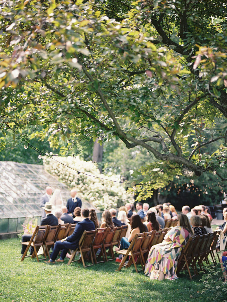 Guests seated under trees watching the ceremony at the greenhouse wedding venue in Michigan.