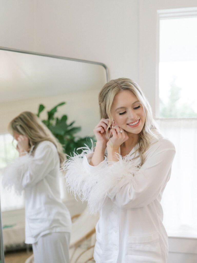 Bride putting on earrings in front of the mirror in her bridal suite.