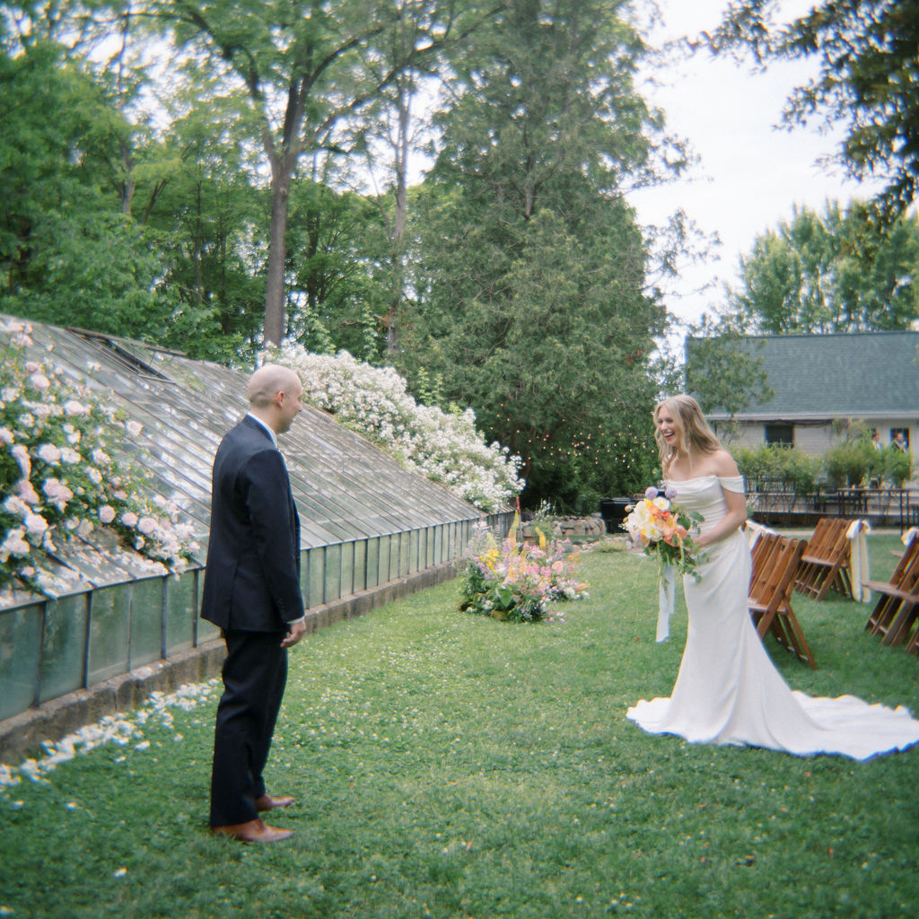 Bride walking toward groom for their first look surrounded by garden flowers.