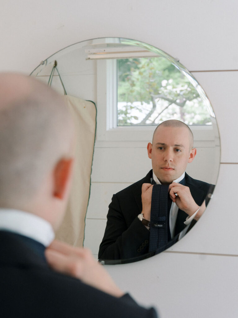 Groom adjusting his tie in the mirror while getting ready.