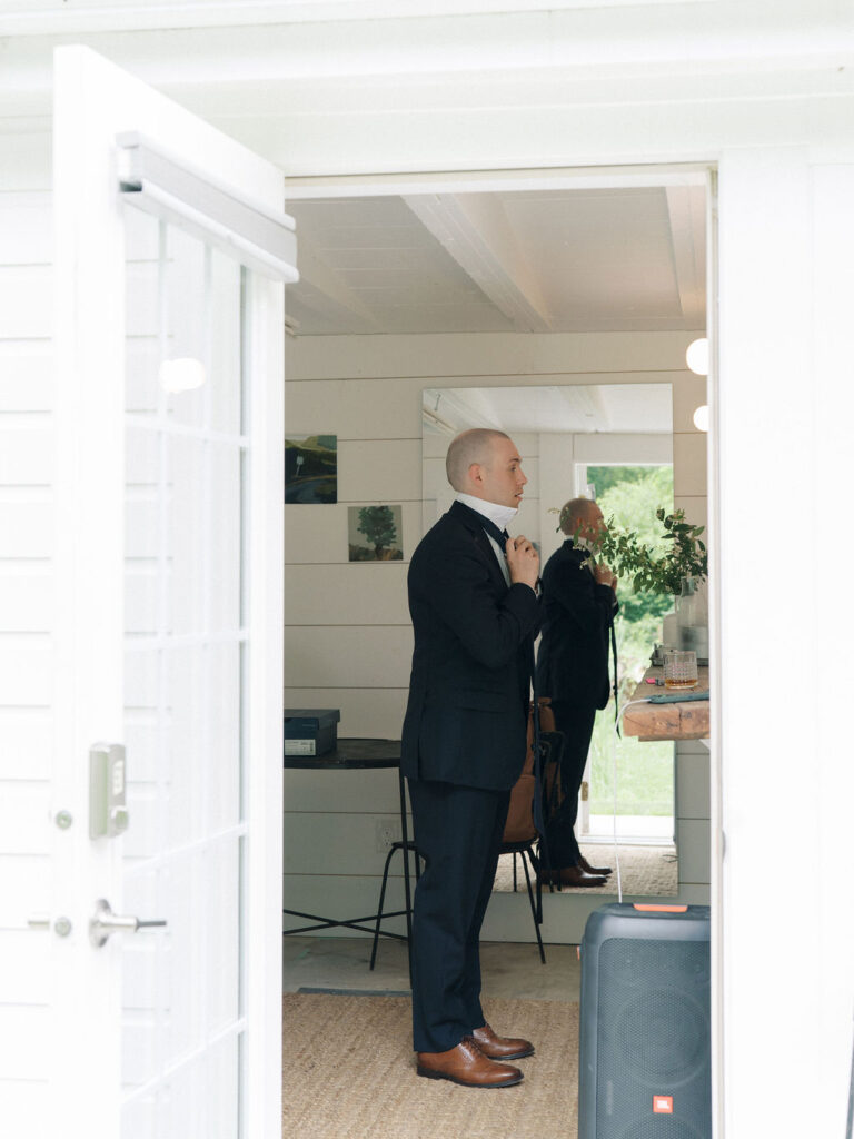 Groom fixing his tie near the doorway of the groom’s cottage.