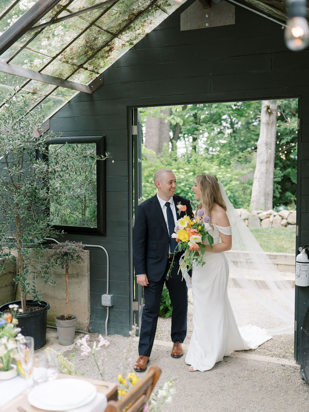 Bride and groom walking in fore their wedding reception room reveal in the greenhouse at Glass House Community