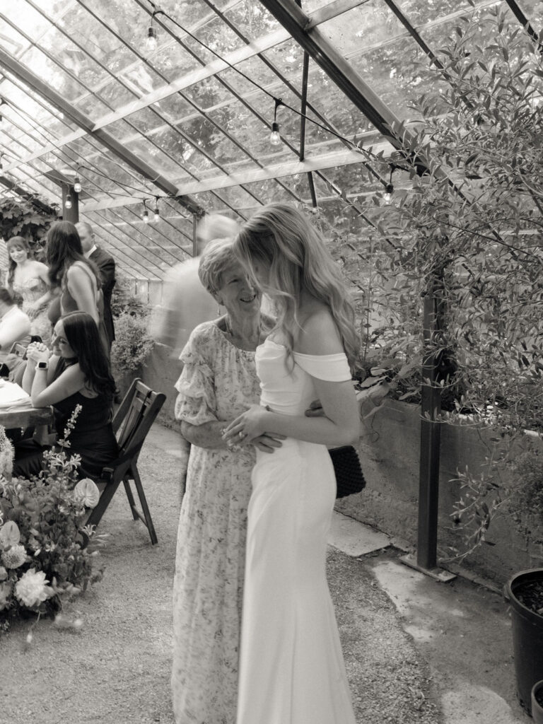 Bride hugging her grandmother inside the greenhouse reception space.