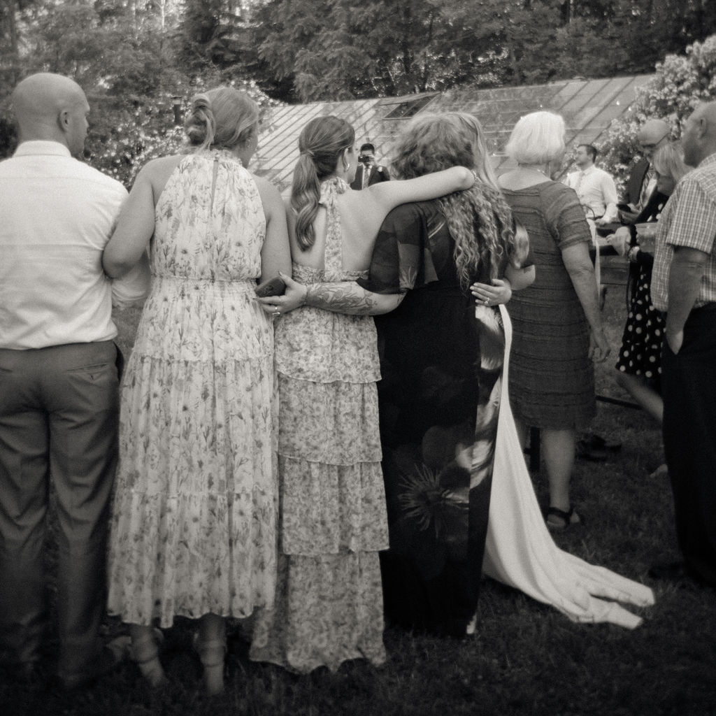 Candid black and white photo og guests hugging during a Glass House Community wedding reception