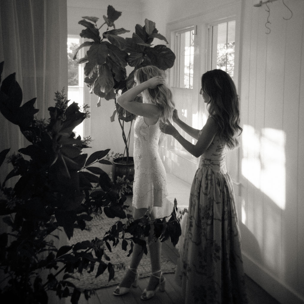 Black and white photo of a bridesmaid helping the bride change into her reception dress