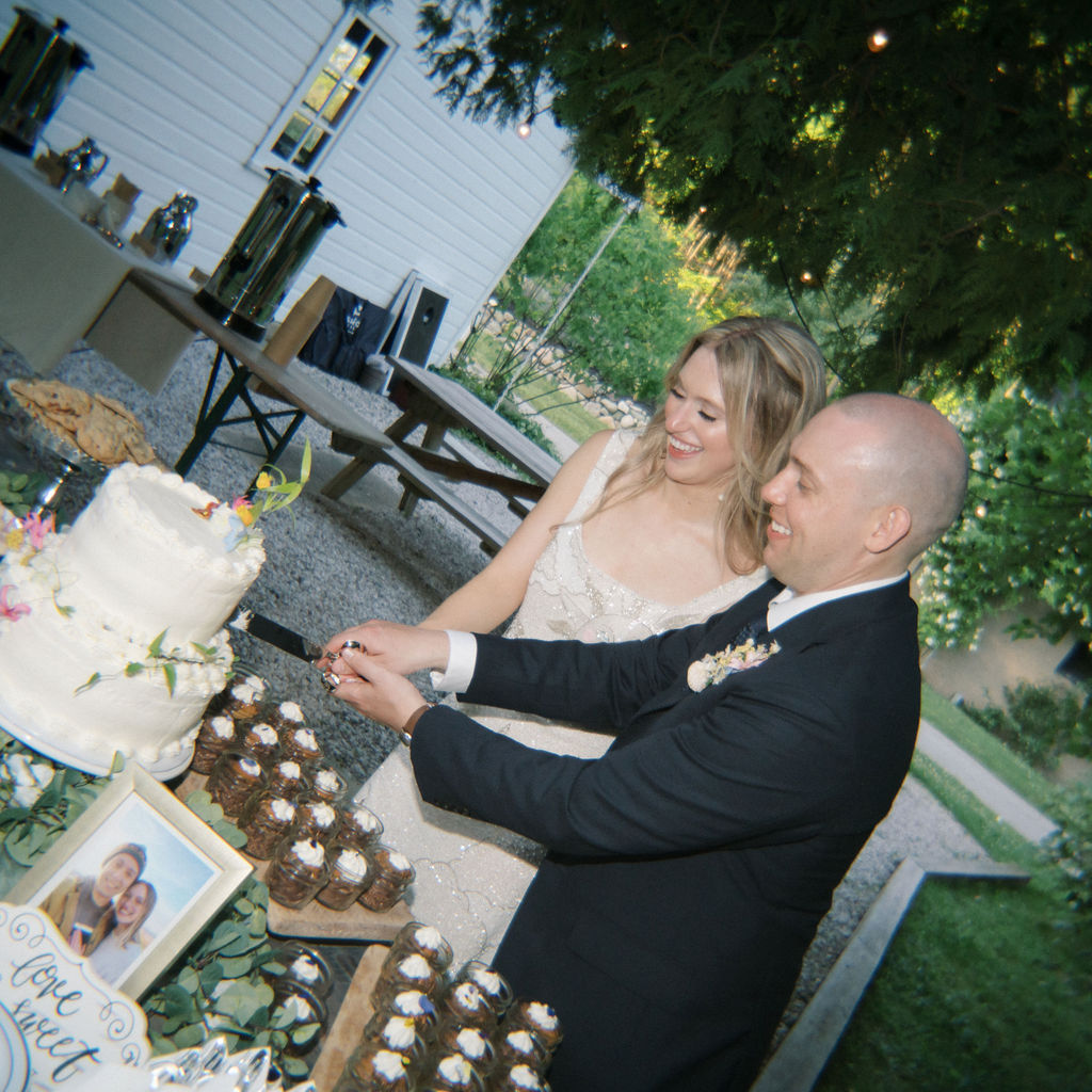 Bride and groom cutting their wedding cake outdoors in the evening light.