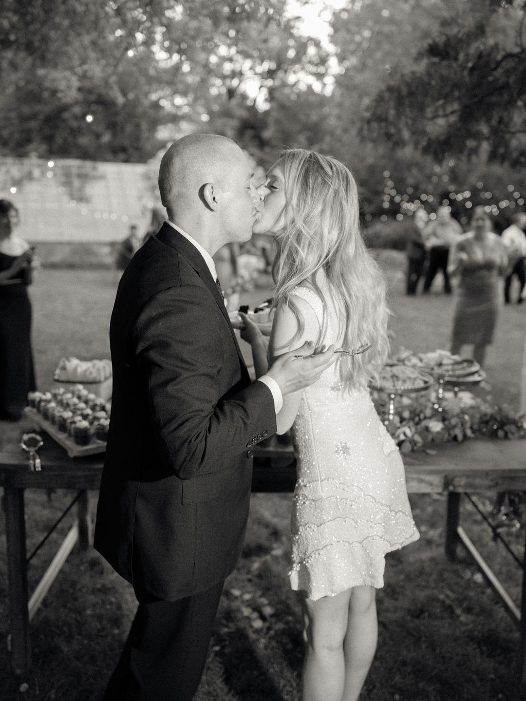 Black and white photo of a bride and groom kissing after cake cutting