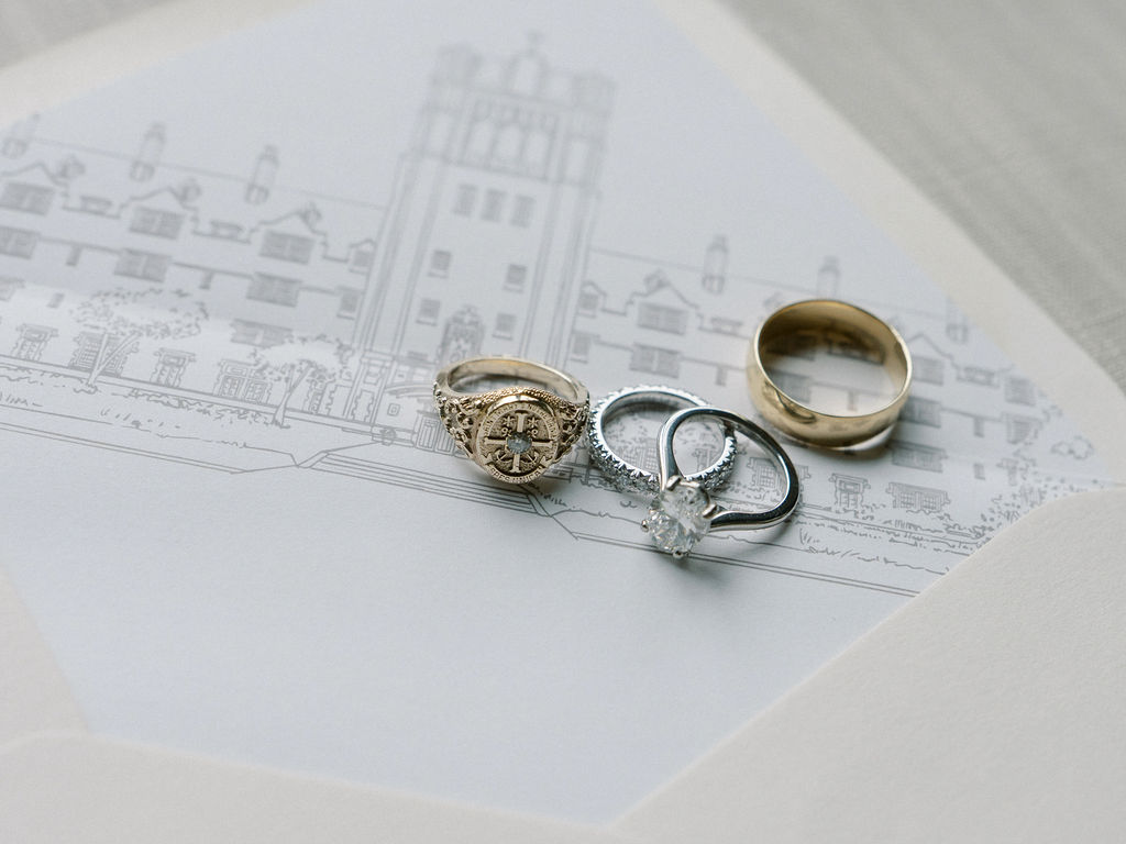 Wedding rings, a band, and College ring laying on a Notre Dame wedding invitation