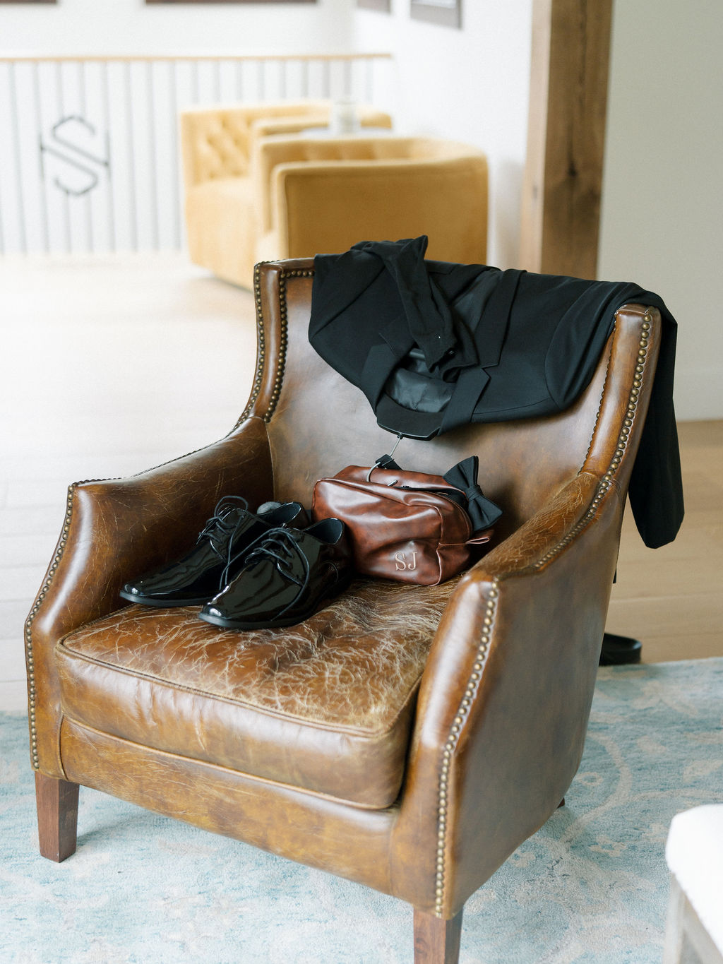 Grooms wedding detail shot with his shoes, bag, and tux laying on a chair