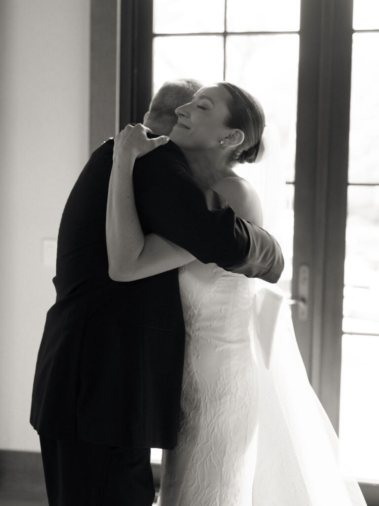 Black and white photo of a bride hugging her father after sharing a first look with him