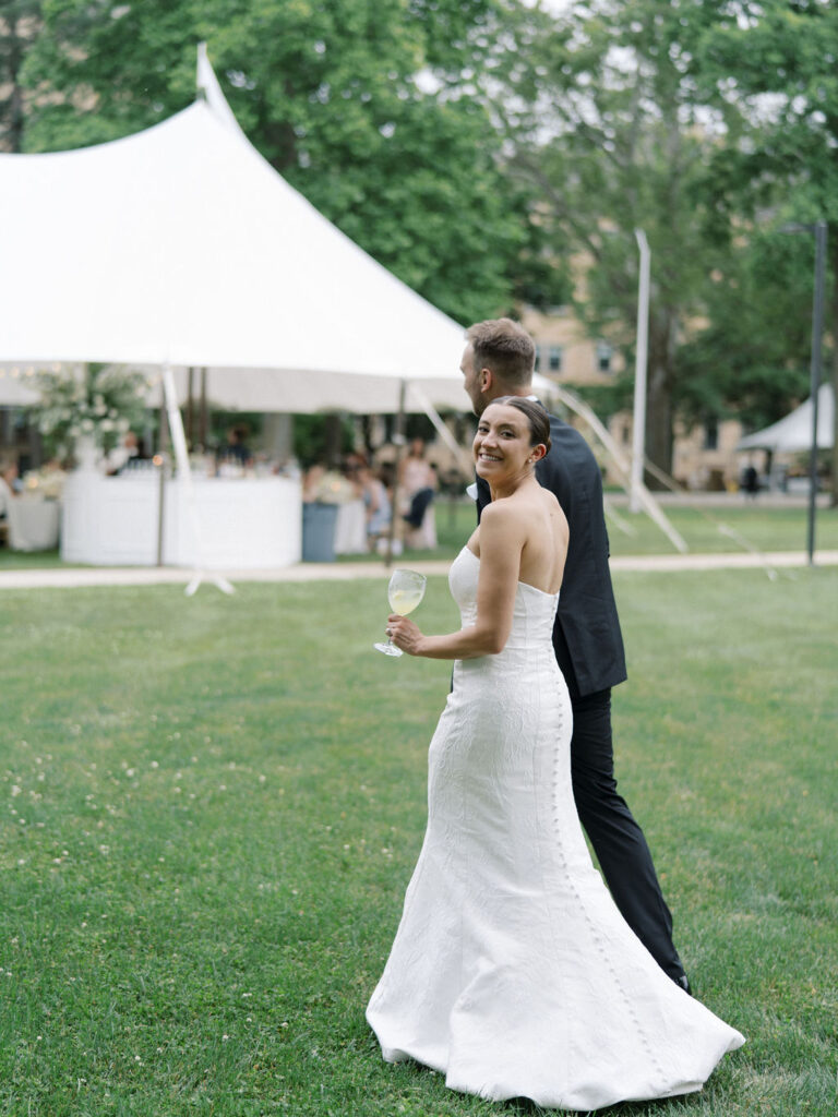 Bride and groom walking back to their tented Saint Mary’s Notre Dame wedding reception setup behind Le Mans Hall