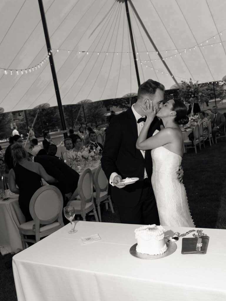Black and white photo of a bride and groom kissing after cake cutting